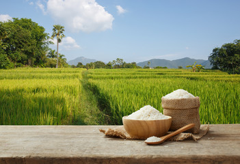 Jasmine rice in bowl and sack on wooden table with the rice field background