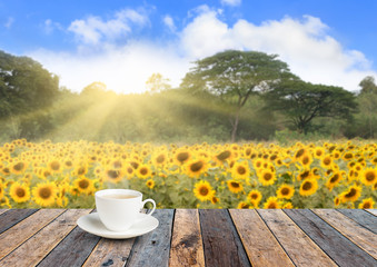 Cup of tea on the wooden floor with sunflower garden background blurred