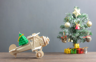 Toy wood airplane transfer fir tree with Blur Christmas tree & many beautiful gift box also essential decoration accessory.Variety objects on modern rustic brown wooden plank and blur grey background.