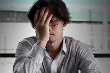 Front view of frustrated stressed young Asian business man covering face with hands and feeling tired with job.