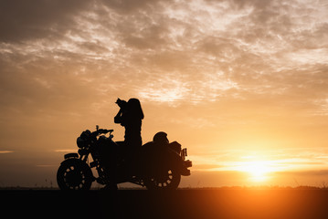 Silhouette of young woman biker take photo and motorcycle on the street at sunrise.Motorbike travel concept