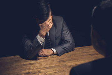 Suspect businessman displaying regret  in dark interrogation room