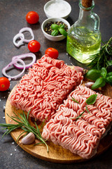 Minced beef and pork on a cutting board, raw meat and various spices on a stone or slate background.