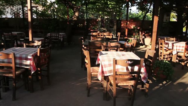 Chairs and tables in typical outdoor Greek tavern in morning sunlight with shadows.