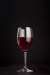 Wine glass with red wine on elegant dark black wooden background, copy space, vertical. Template for portfolio, advertising, design, branding identity, cover magazine, bar and restaurant menu.
