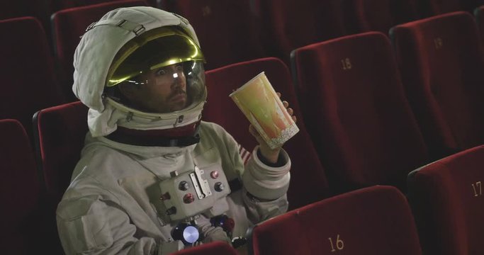 A movie astronaut looks at a movie while eating pop corn and enjoying the movie. Concept of: cinema and space films, film of the other world, surreal situations.