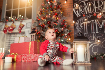 Baby first Сhristmas. Beautiful little baby boy celebrates Christmas, New Year's holidays.Cute Toddler playing and smilingnear gifts, tinsel, balls and christmas tree