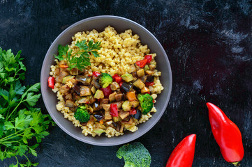 Light healthy dietary vegan dish: couscous and vegetables (zucchini, eggplant, carrots, sweet peppers, onions, parsley) on a black background. The top view.