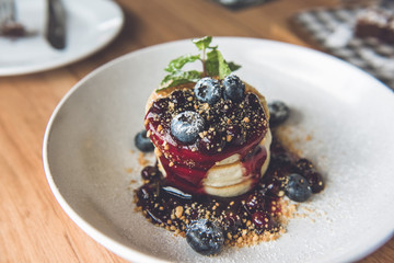 Beautiful appetizing stack of fluffy pancakes topped with fresh blueberries, syrup and ground biscuit