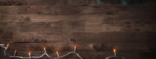 Christmas decorative light with green pine leaves on wood table, banner background - Powered by Adobe