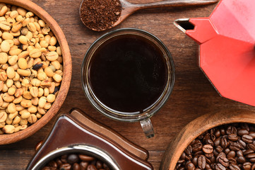 Coffee beans with ground coffee in wooden spoon and red kettle on the side on wooden background