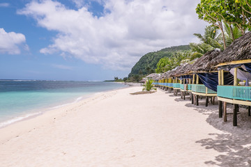 View along Lalomanu Beach, Upolu Island, Samoa, of thatched open-sided Samoan beach fale huts that are an alternative to hotel or resort accommodation