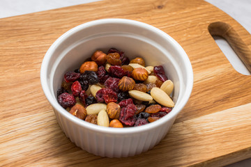 Mixed nuts with cranberries and raisins in white bowl on cutting board