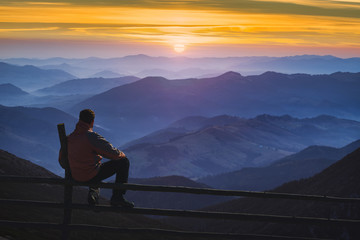 Man hiker sitting on a fence and enjoying the sunrise