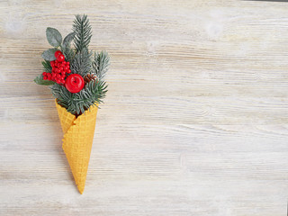 New year's concept of the waffle cone and artificial fir twigs with red berries of different sizes on a light wooden background.