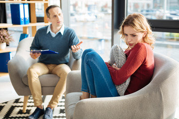 Obraz premium Feeling of stress. Sad unhappy young woman sitting in the armchair and hugging a pillow while having stress
