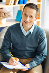 Not to forget. Positive delighted handsome man holding his notes and writing in them while smiling