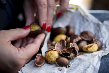 Mädchen mit roten Fingernägeln schält Kastanien ab, Zeitungspapier mit Kastanien, Finger unscharf im Vordergrund