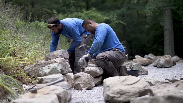 Hammering at a rock to make it fit better into a stone wall design.