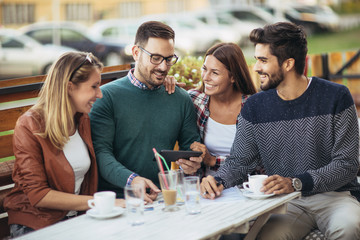 Group of four friends having fun a coffee together. Two women and two men at cafe talking laughing and enjoying their time