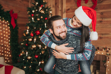 Merry Christmas and Happy New Year!. Young couple celebrating holiday at home. Man giving piggyback to women