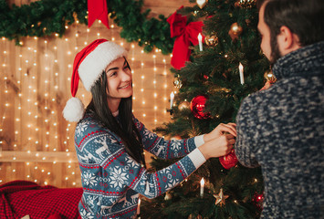 Merry Christmas and Happy New Year!. Young couple celebrating holiday at home. Young woman and woman decorate the New Year tree
