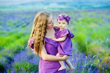 Mother hugs her little daughter in the rays of the setting sun, wearing long lilac dresses