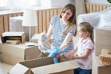 Pretty young mother and her cute little daughter having fun while sitting on floor of new apartment...