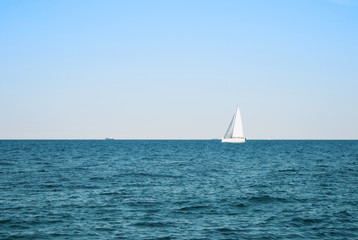 Sea lake ocean water landscape with dark waves and a lonely white yacht at the horizon on sunny day.