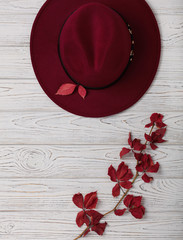 Hat burgundy color on a gray wooden background with autumn red leaves.