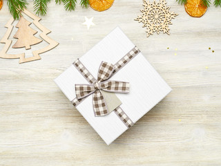 Christmas background. Square gift box with bow. The branches of fir, dried orange, star foil, fir cone, wooden toys in the shape of Christmas trees and snowflakes