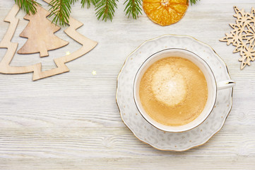 Christmas background. Top view of cappuccino coffee in a white Cup on a wooden table. Fragments of wooden toys, Christmas trees and snowflakes, the branches of fir, dried orange slice.