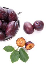 Steel colander with ripe plums, whole and half ripe plums with leaf isolated on a white background..