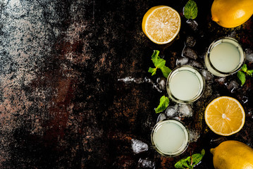 Traditional italian alcoholic homemade beverage, lemon liqueur limoncello with fresh citrus, ice and mint, on rusty black table, copy space top view