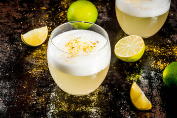 Peruvian, Mexican, Chilean traditional drink pisco sour liqueur, with fresh lime, on rusty black table, copy space