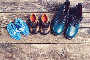 Different children's shoes on dark wooden background. Baby's knitted shoes and leather kid's boots for cold weather.