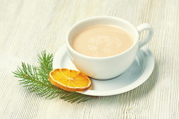 Coffee Cup cappuccino and saucer on a light wooden background decorated with fir branch and dried orange slice. Christmas morning.