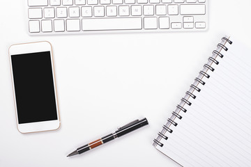 Top view of smartphone and computer keyboard next to notebook and pen on white background. Isolated.