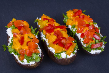 Vegetarian healthy food - eggplants stuffed with cream cheese, green herbs, grilled red and yellow peppers on a black slate background
