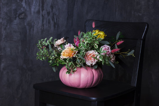 Autumn floral bouquet in pumpkin vase on black chair