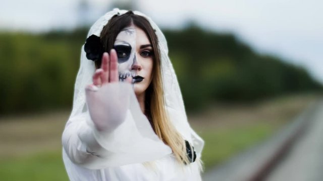 The portrait of young woman with spooky make-up for Halloween in a white bride dress. 4K
