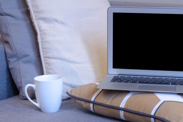 laptop and cup stand on sofa, pillows, coffee and notebook 
