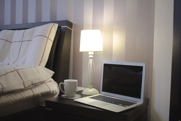 laptop in bedroom with bed, lamp and home decor background.