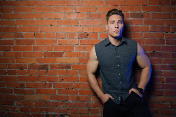 Muscular man Posing against a red brick wall. Standing In a checkered sleeveless shirt.