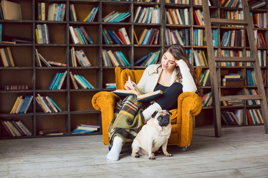 Education and reading books. Young woman sitting in the library with her small pug dog. Literature time