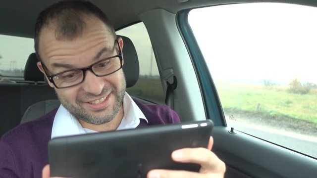Businessman sits in the car, looking at the tablet screen at good results. Happy adult man looking surprised. Positive human emotion.