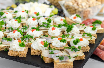 Slices of rye bread wheat bread with herring pieces sprinkled with green onion on a black granite plate. The bacon is milled in a meat grinder on a toast a piece of bread. Buffet snack menu for beer.