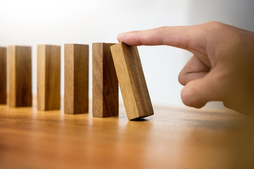 Hand of business man pushing dominoes for start on wooden background Planning risk and strategy...