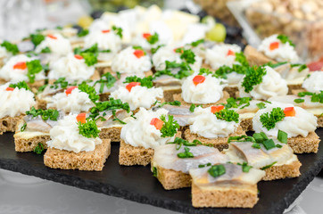 Slices of rye bread wheat bread with herring pieces sprinkled with green onion on a black granite plate. The bacon is milled in a meat grinder on a toast a piece of bread. Buffet snack menu for beer.