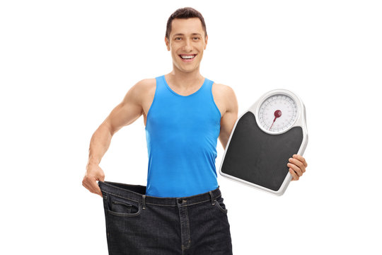 Guy in pair of oversized jeans holding a weight scale